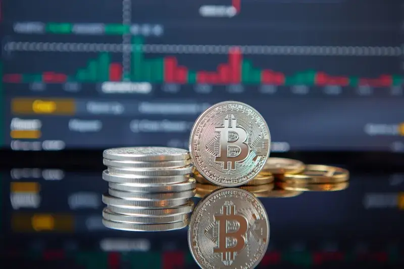Stack of Bitcoin coins in front of a stock market graph, reflecting cryptocurrency trends.