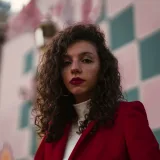 Candid portrait of a woman in a red jacket with a geometric mural background captured in Buenos Aires.