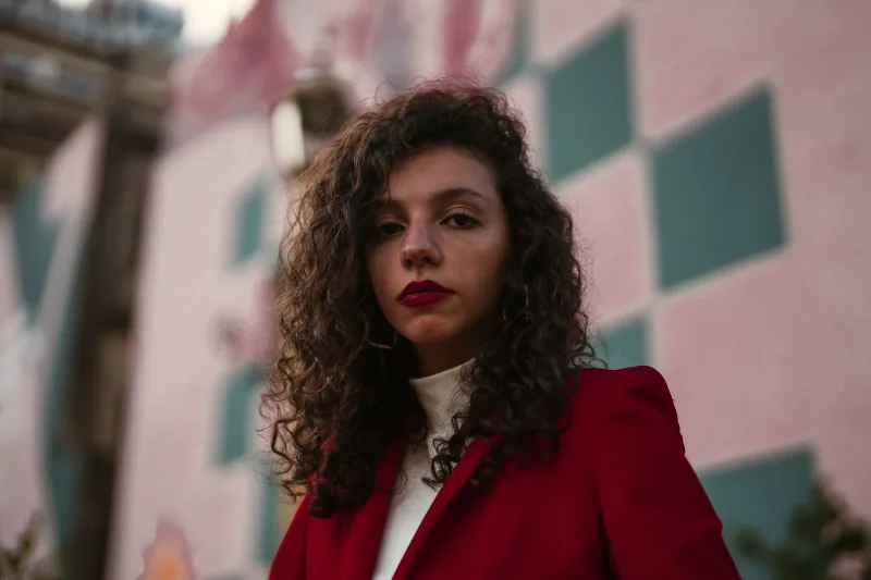 Candid portrait of a woman in a red jacket with a geometric mural background captured in Buenos Aires.