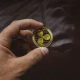 A close-up of a hand holding a gold Ripple cryptocurrency coin, symbolizing digital currency concept.