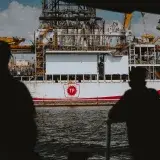 Silhouetted figures observing a large offshore oil rig at sea, emphasizing maritime industry.