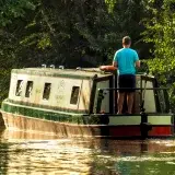 Serene summer scene of a man cruising a narrowboat along a verdant canal in Trevor, Wales.