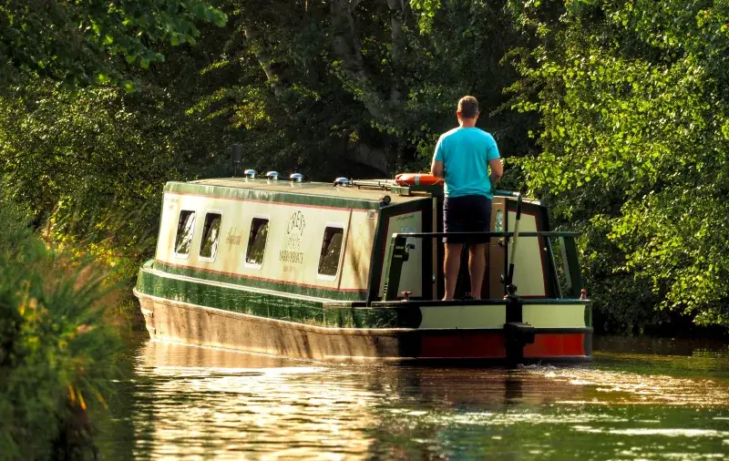 Serene summer scene of a man cruising a narrowboat along a verdant canal in Trevor, Wales.