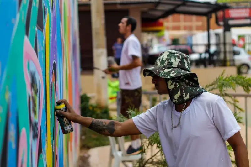 Two artists painting a vibrant graffiti mural on a public wall outdoors in Brasil.