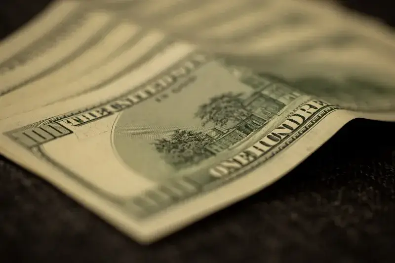Detailed shot of multiple US hundred dollar bills fanned out on a flat surface, symbolizing wealth.