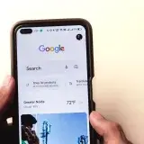 Un primer plano de una mano sosteniendo un smartphone con la búsqueda de Google mostrada en la pantalla.