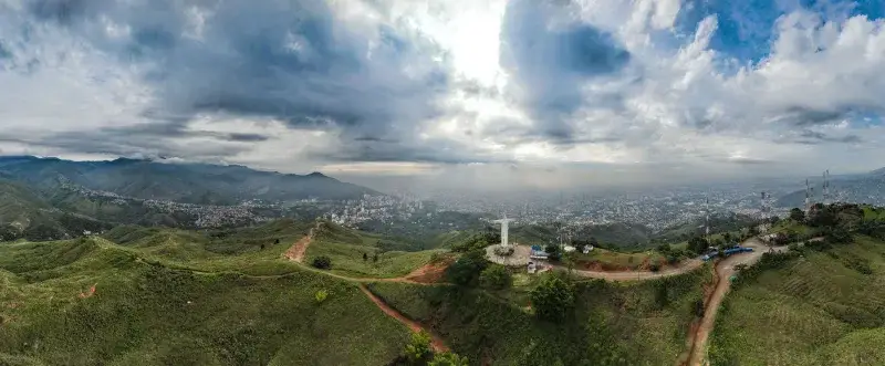 Stunning aerial panorama of Cali, Colombia featuring Cristo Rey statue under dramatic skies.