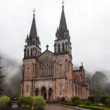 Misty view of Basilica de Covadonga, a historic landmark in Asturias, Spain, surrounded by lush greenery.
