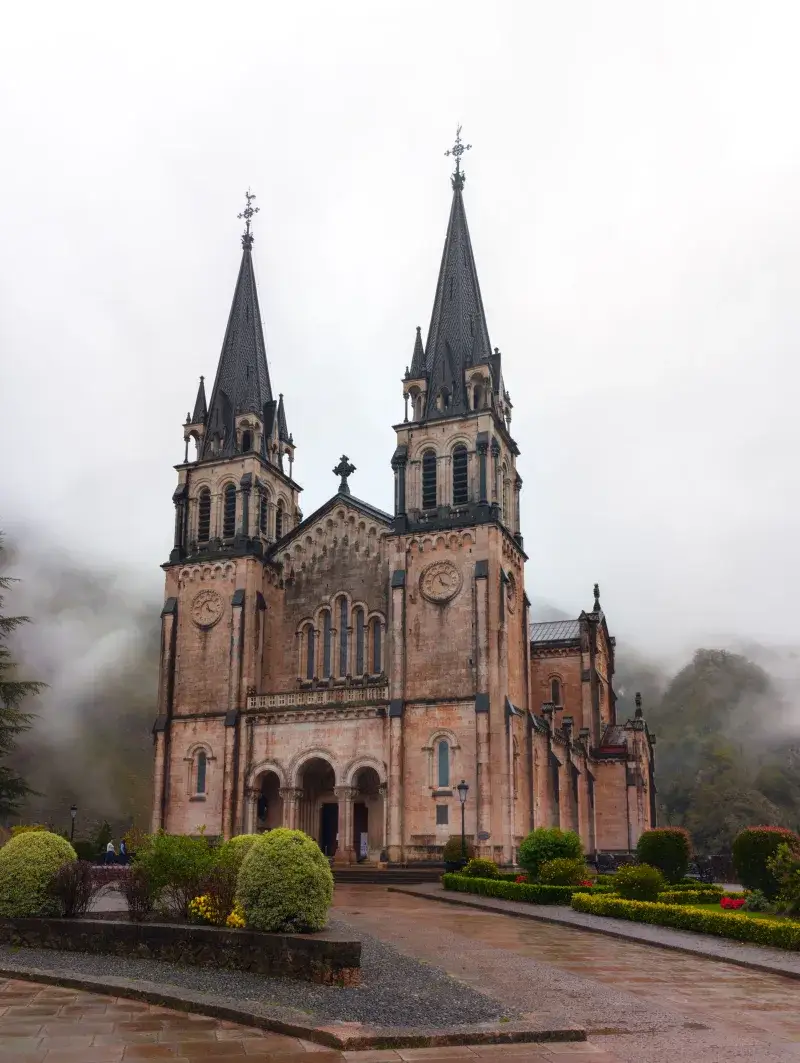 Misty view of Basilica de Covadonga, a historic landmark in Asturias, Spain, surrounded by lush greenery.
