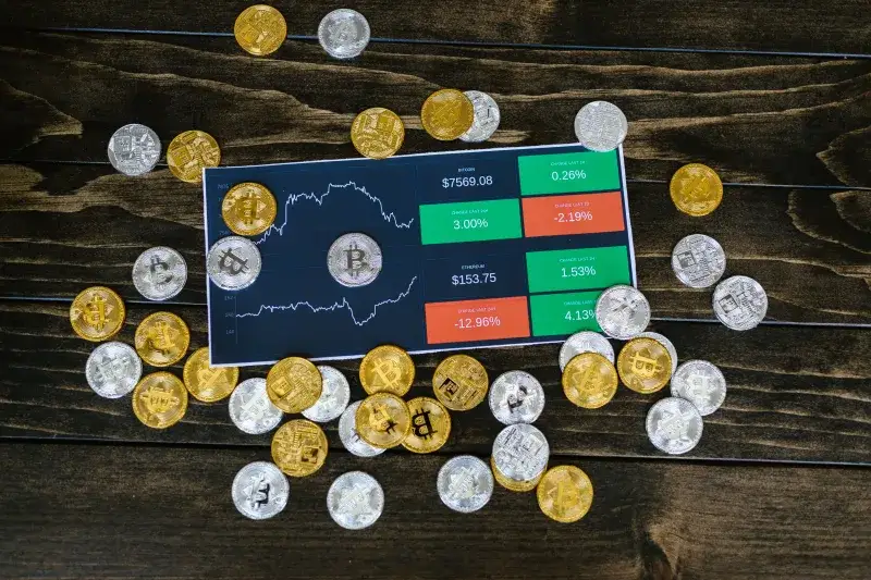 Monedas de Bitcoin dispersas alrededor de un gráfico de acciones en una mesa de madera oscura, simbolizando la inversión en criptomonedas.
