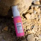 Close-up of SPF 50+ sun cream bottle with pink toned packaging on rocky surface.