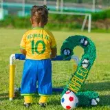 A young child wearing a Neymar Jr. jersey stands by a mini soccer goal on a grassy field.