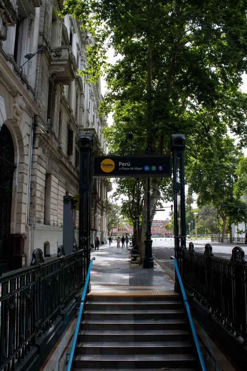 Escena urbana de la entrada de la estación de metro Perú en Buenos Aires con árboles bordeando la calle.