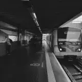 Black and white image of a metro station with a train arriving and commuters in view.