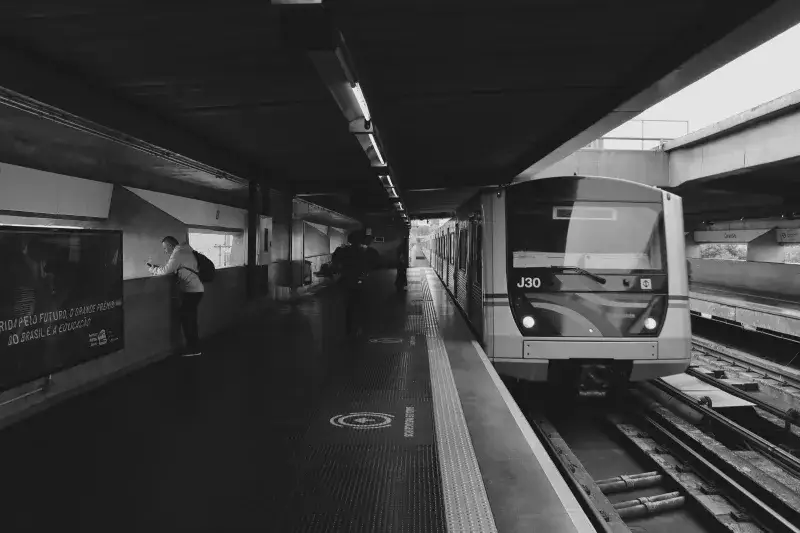 Black and white image of a metro station with a train arriving and commuters in view.