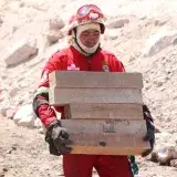 Rescue worker in red uniform carrying wooden planks in a rocky area in Moquegua, Peru.