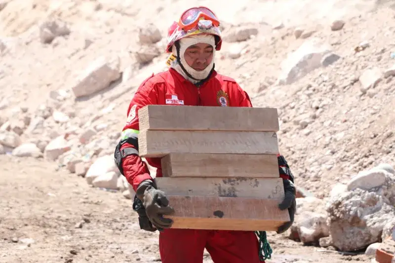 Rescue worker in red uniform carrying wooden planks in a rocky area in Moquegua, Peru.