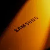 Dramatic close-up of a Samsung electronic device highlighted by golden lighting and shadows.