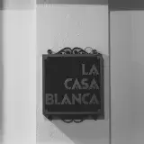Black and white photograph of a La Casa Blanca sign mounted on a textured wall, emphasizing architecture.