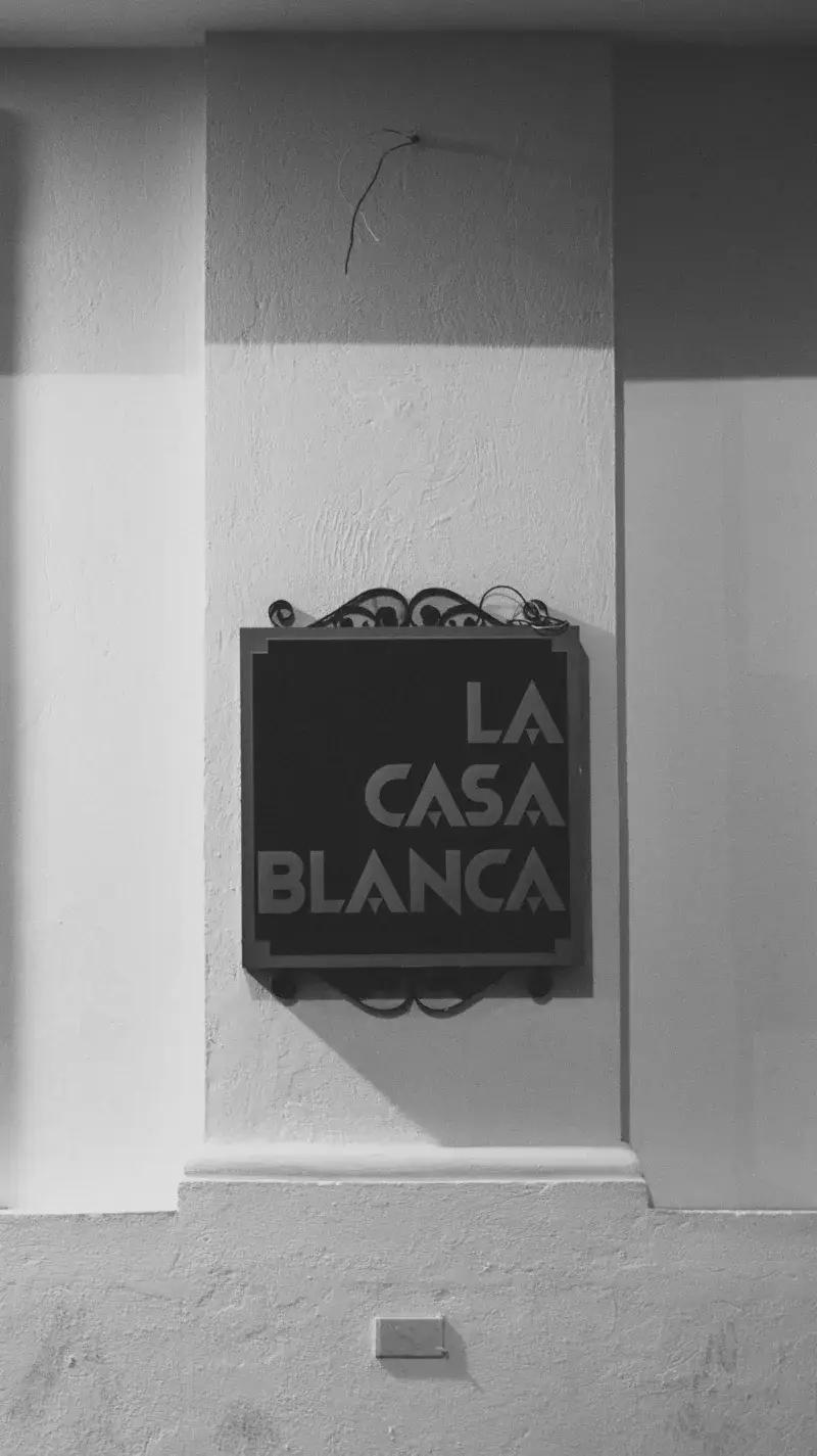 Black and white photograph of a La Casa Blanca sign mounted on a textured wall, emphasizing architecture.