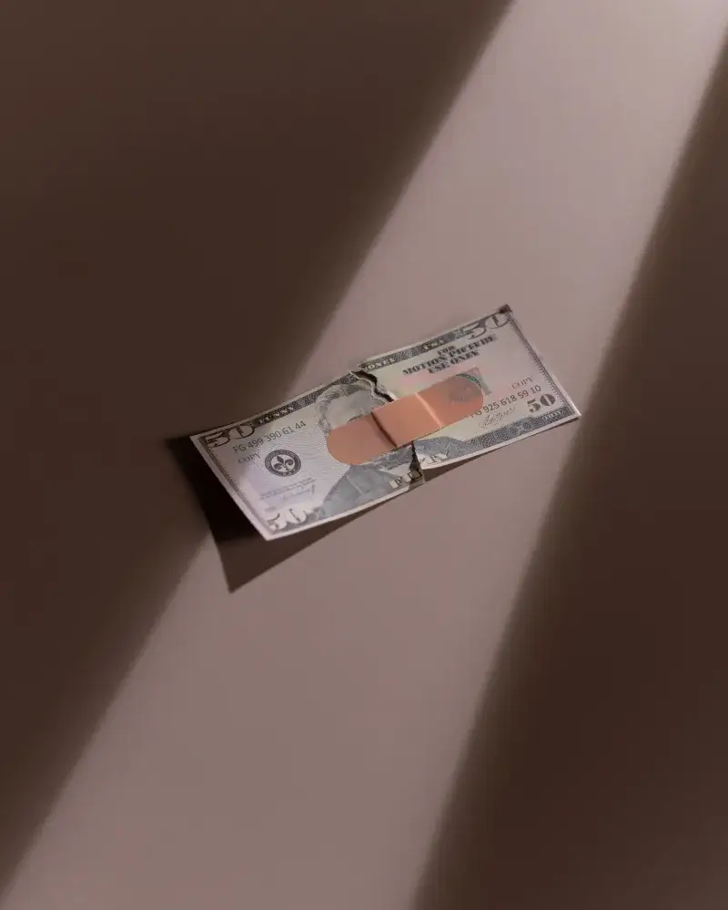 A torn dollar bill patched with a bandage, symbolizing financial recovery.