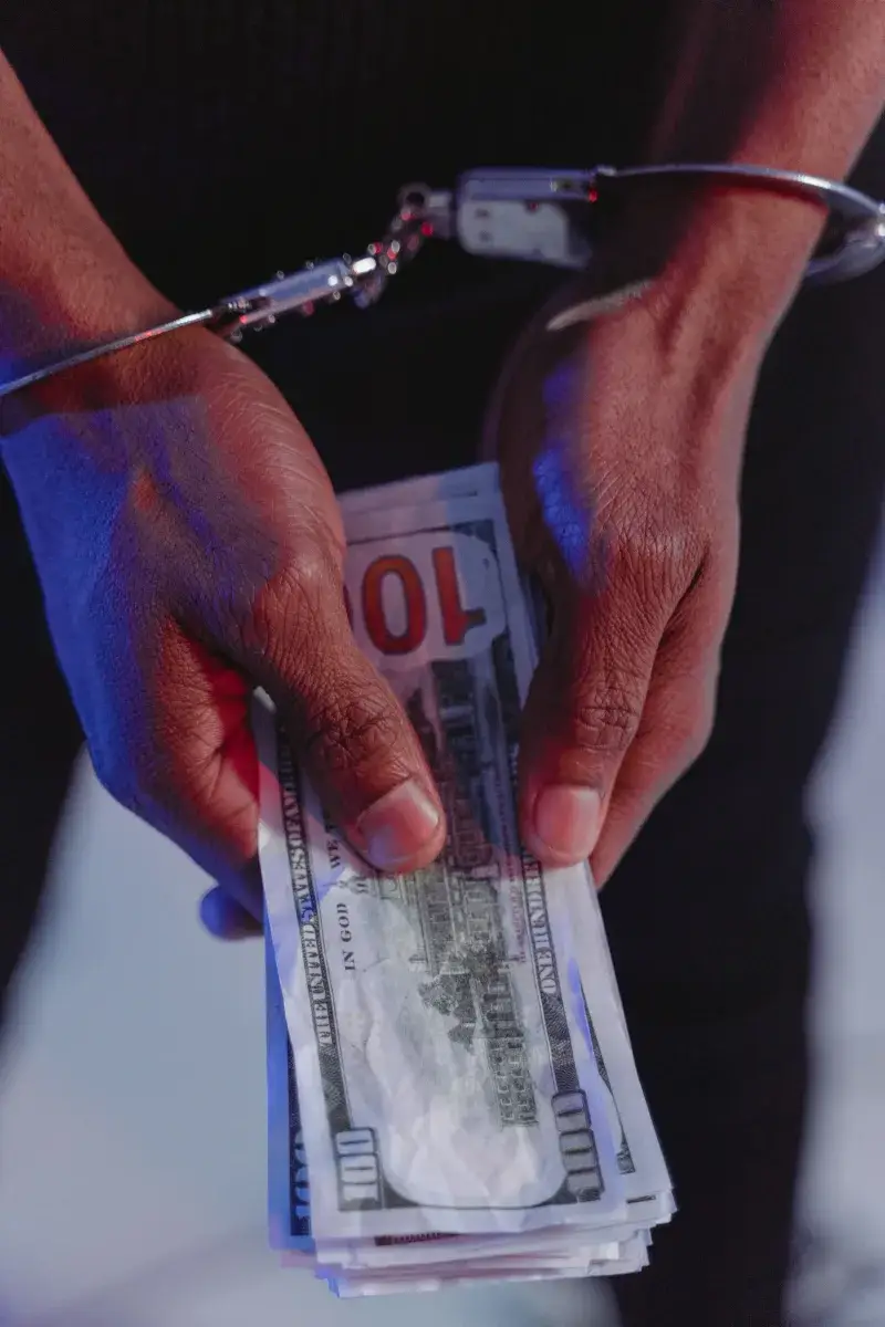 Close-up of handcuffed hands holding US dollars, symbolizing financial crime.