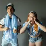 Two enthusiastic fans cheer for Argentina's soccer team indoors.