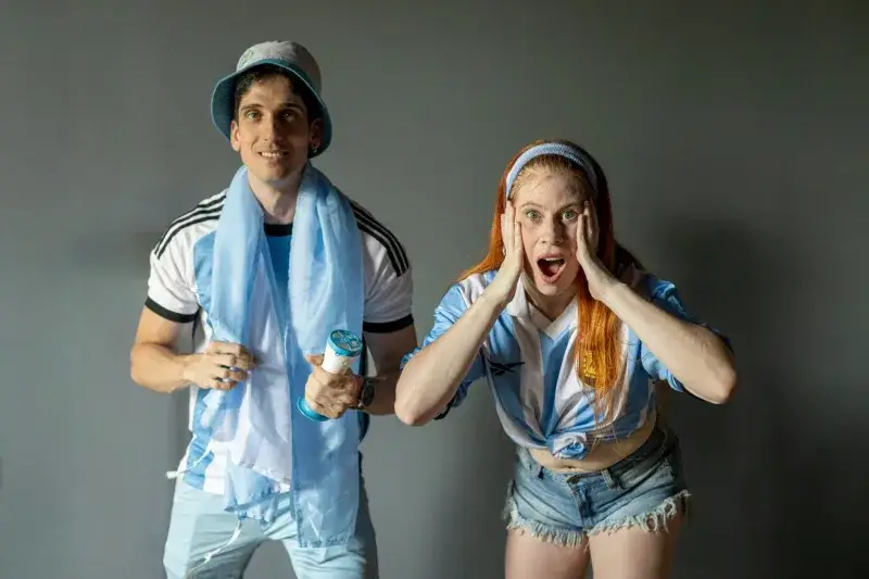 Two enthusiastic fans cheer for Argentina's soccer team indoors.
