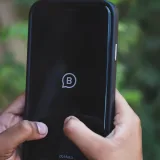 Close-up of hands holding a smartphone with Meta logo outdoors against green background.