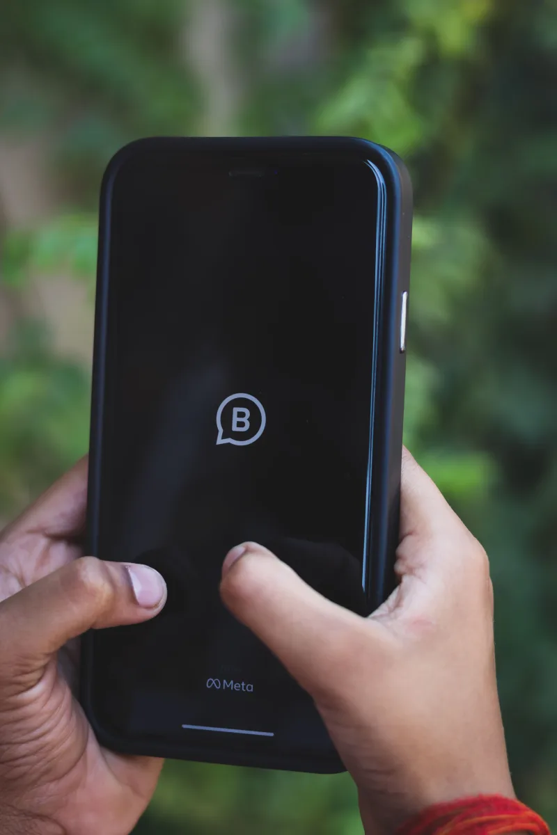 Close-up of hands holding a smartphone with Meta logo outdoors against green background.