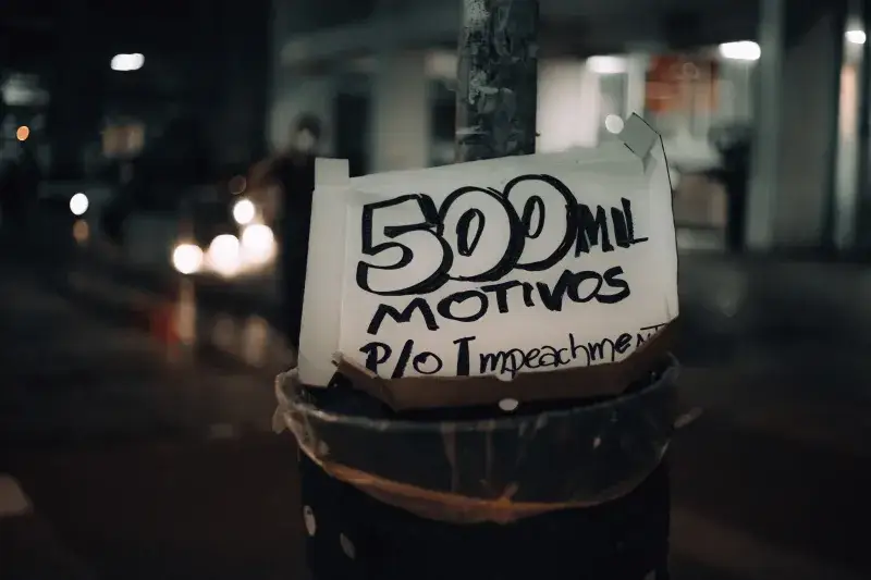 A street pole displaying a protest sign with the message '500 mil motivos p/o impeachment' at night.