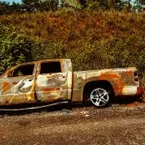 Rusted wreckage of a truck after an automobile fire on the side of the road.