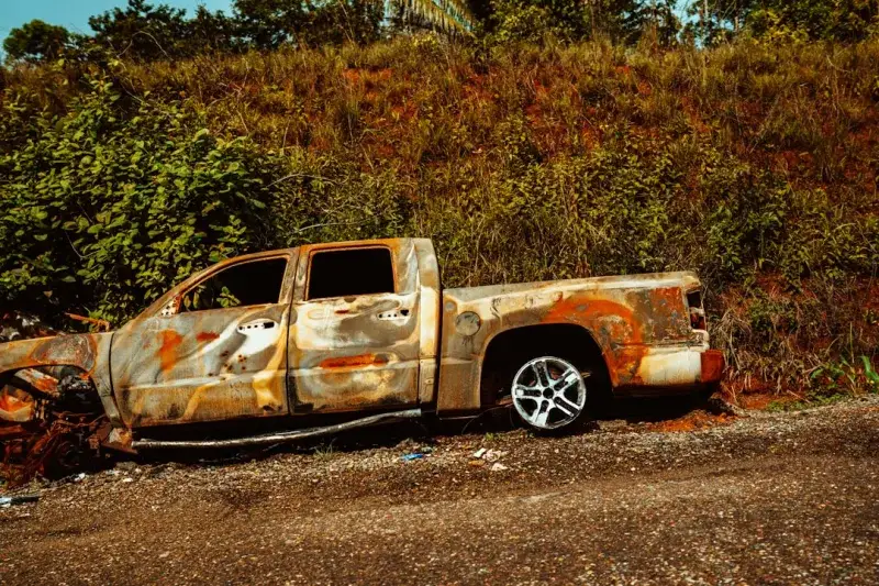 Rusted wreckage of a truck after an automobile fire on the side of the road.