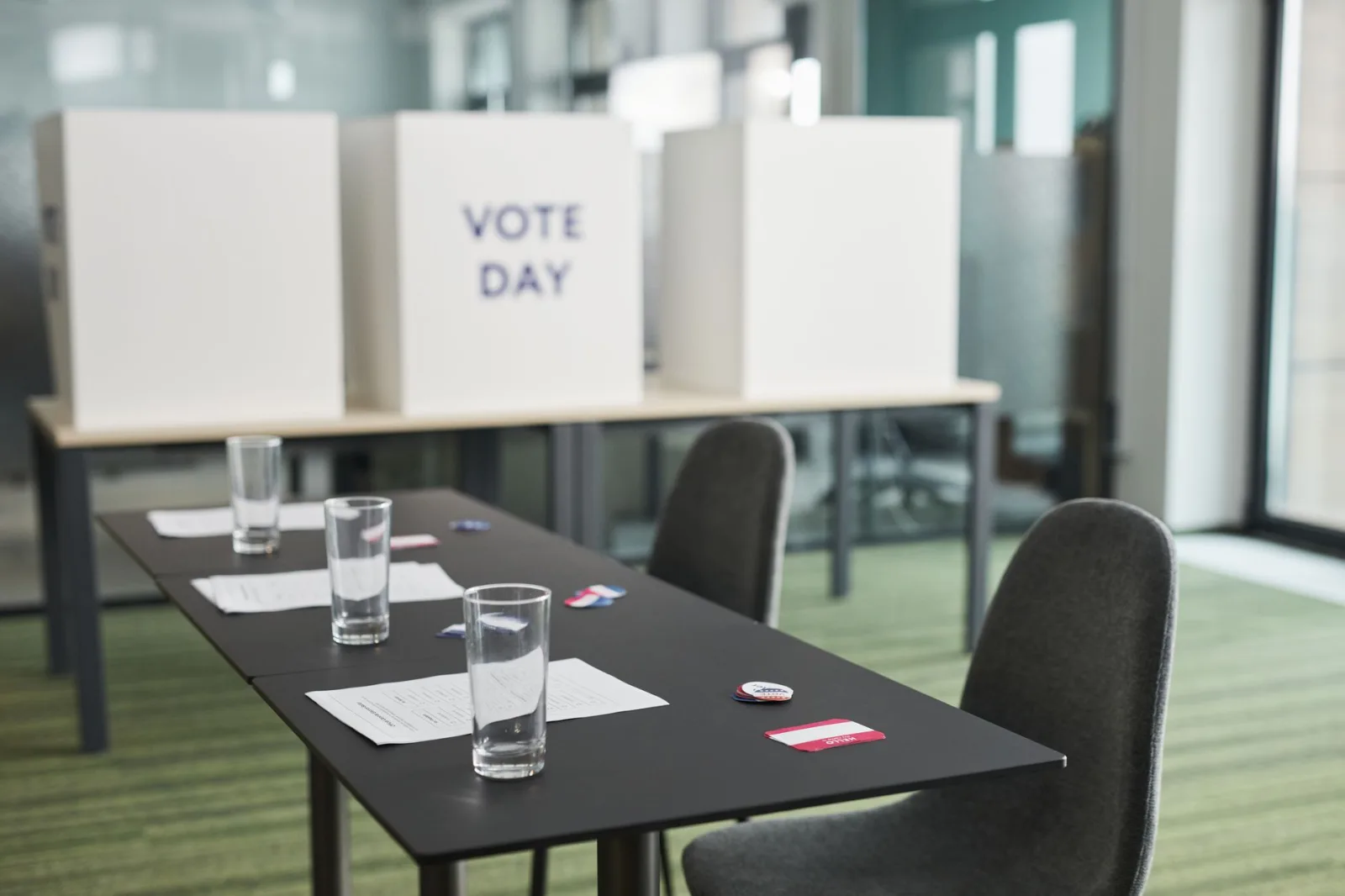 A prepared voting station with tables, chairs, and privacy booths in a conference room.