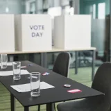 A prepared voting station with tables, chairs, and privacy booths in a conference room.
