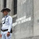 A guard in uniform stands by a historic building in Manila. Street sign reads 'Gral. Luna Real De Palacio'.
