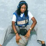 Teen girl wearing headphones, Nuggets jersey, holding basketball outdoors.