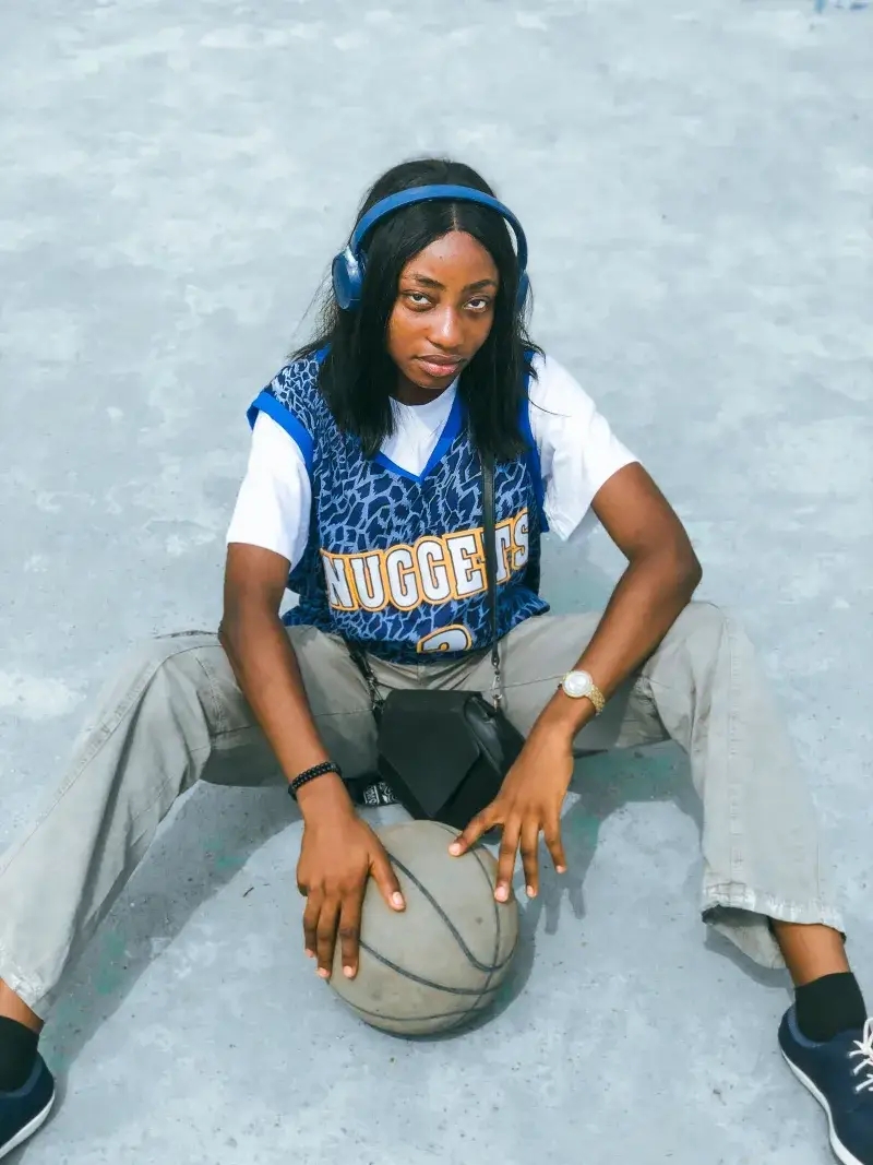 Teen girl wearing headphones, Nuggets jersey, holding basketball outdoors.