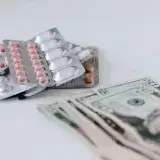 Multicolored pills in silver blisters on white surface near heap of paper money representing expensive pharmacy