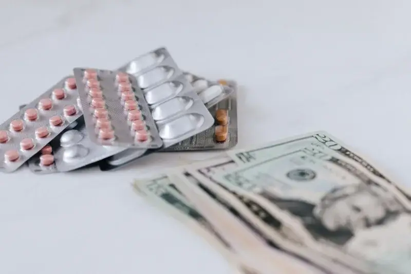 Multicolored pills in silver blisters on white surface near heap of paper money representing expensive pharmacy