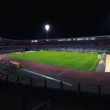 Brightly lit empty soccer stadium with green field under spotlights during night time.