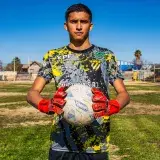 Portrait of a young soccer player holding a ball on a sunny outdoor field.