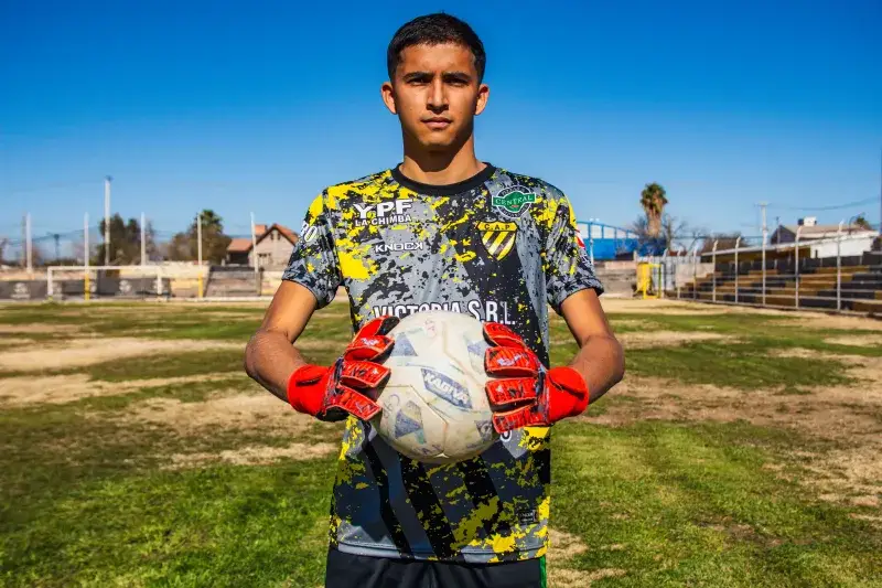 Portrait of a young soccer player holding a ball on a sunny outdoor field.