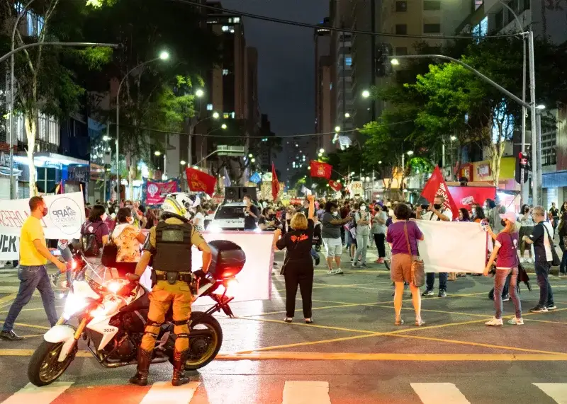 Vibrant urban protest scene at night with diverse crowd and police officer in foreground.