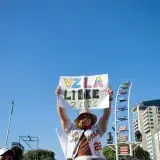 A person holds a sign reading 'VZLA Libre 2026' in a peaceful protest with a city backdrop.