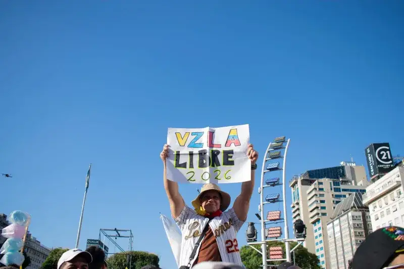 A person holds a sign reading 'VZLA Libre 2026' in a peaceful protest with a city backdrop.