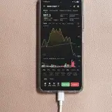 Smartphone mostrando el gráfico de negociación BNB/USDT con el cable de carga conectado.