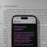 Smartphone showing OpenAI ChatGPT in focus, on top of an open book, highlighting technology and learning.
