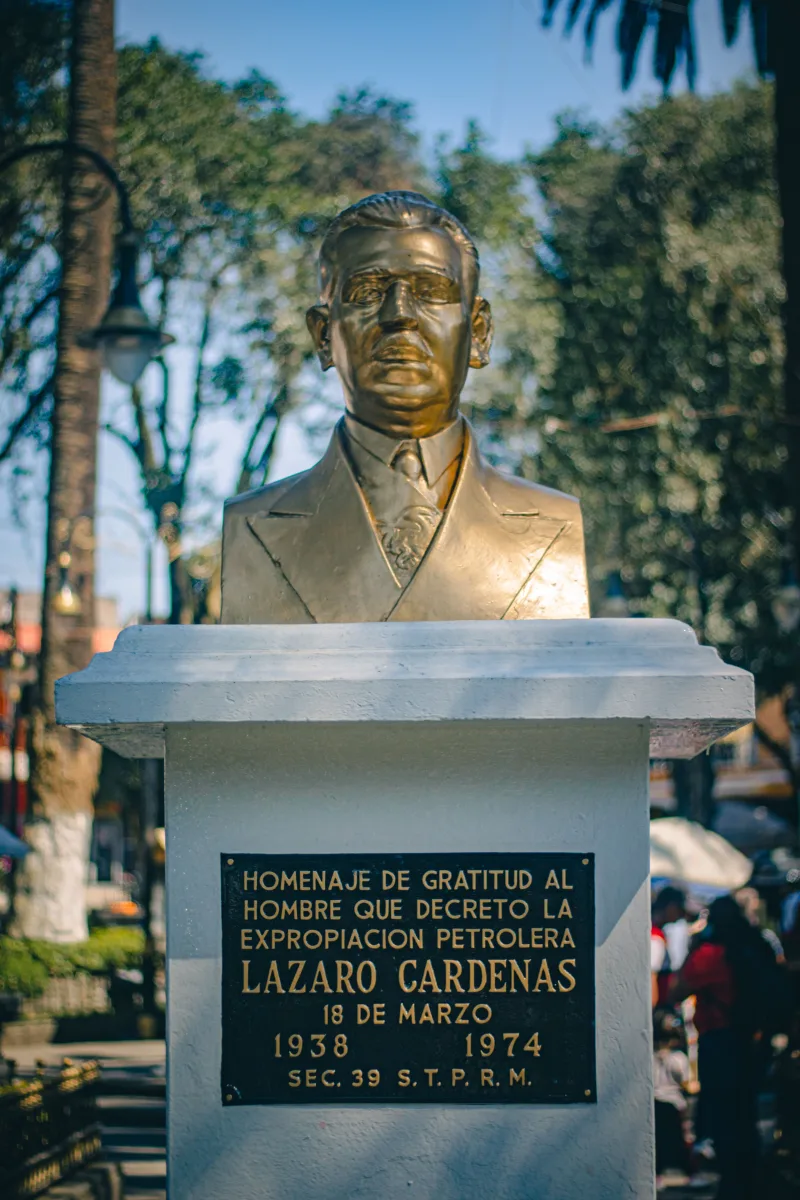 Bronze statue of Lázaro Cárdenas in a sunny Huauchinango park, capturing historical homage.