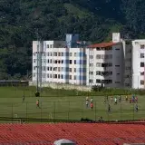 Aerial view of a youth soccer match in a Venezuelan residential area surrounded by lush greenery.